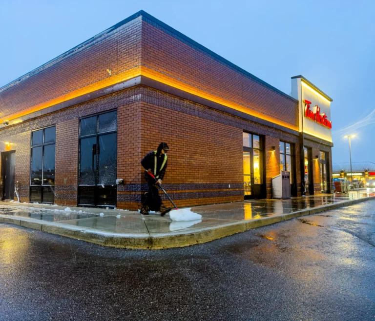 LECM crew member shovelling slush off a storefront walkway at dawn during the first snowfall of the season